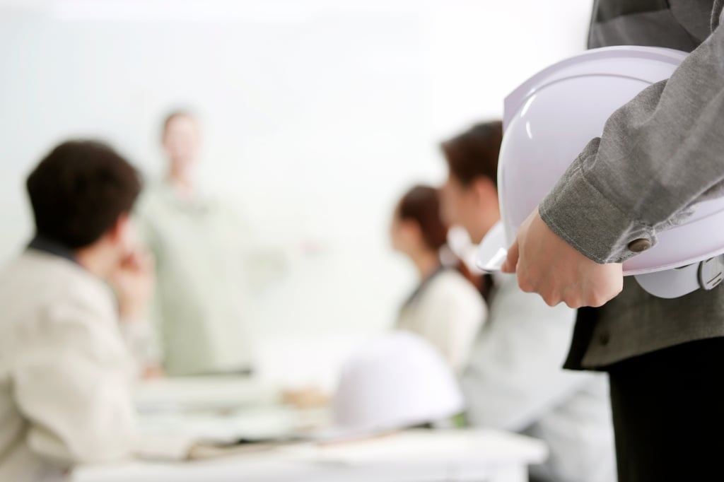 Profissional segurando capacete de segurança em sala de treinamento com equipe ao fundo