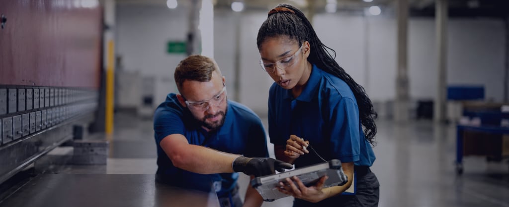 Two factory workers reviewing a tablet in an industrial workshop.