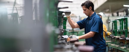 Trabajador operando maquinaria en una planta industrial, representando el Programa de Convergencia Social y Laboral SLCP en entornos de manufactura.