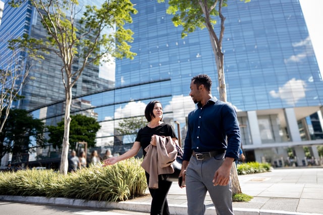Dois profissionais caminhando em frente a edifício corporativo envidraçado em ambiente urbano
