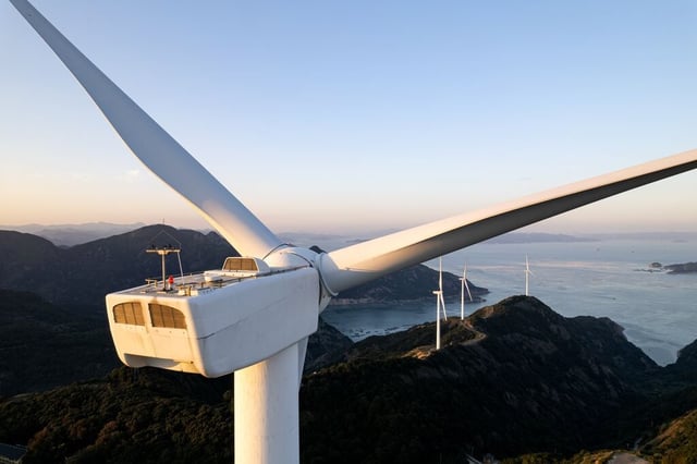 Turbina eólica em destaque com outras ao fundo em paisagem costeira ao entardecer