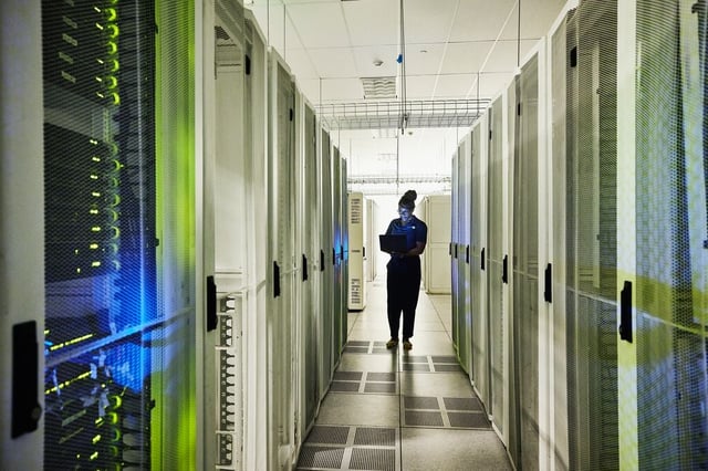 Técnico revisando un centro de datos entre racks de servidores, representando la ciberseguridad y la gestión de riesgos en infraestructura crítica.