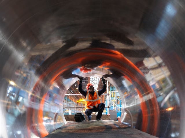 Profissional com capacete e colete de segurança realizando inspeção em instalação industrial
