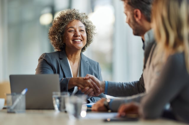 Business handshake in office setting with laptop and observer.