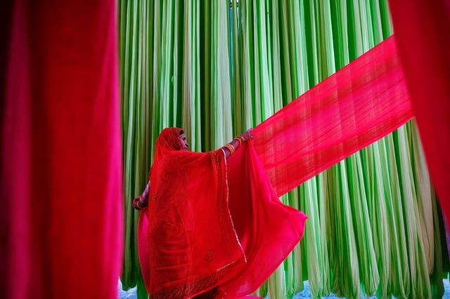 Mulher manuseando tecido vermelho entre faixas têxteis coloridas em processo de produção