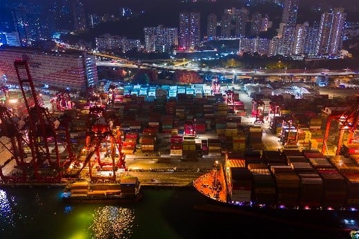 Vista aérea noturna de porto com contêineres, guindastes e operações logísticas